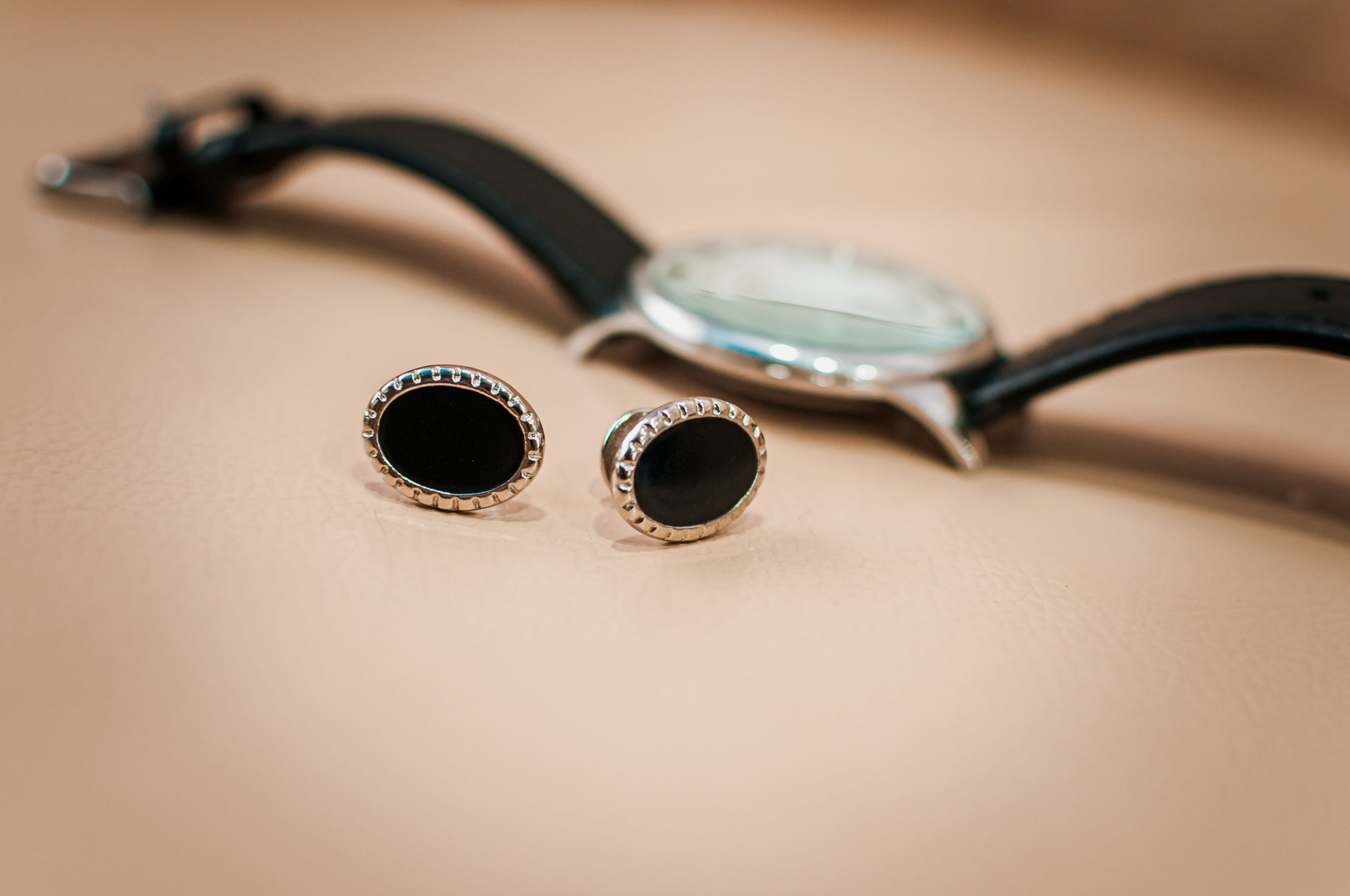 Men's cufflinks and a watch with a black strap on a brown background