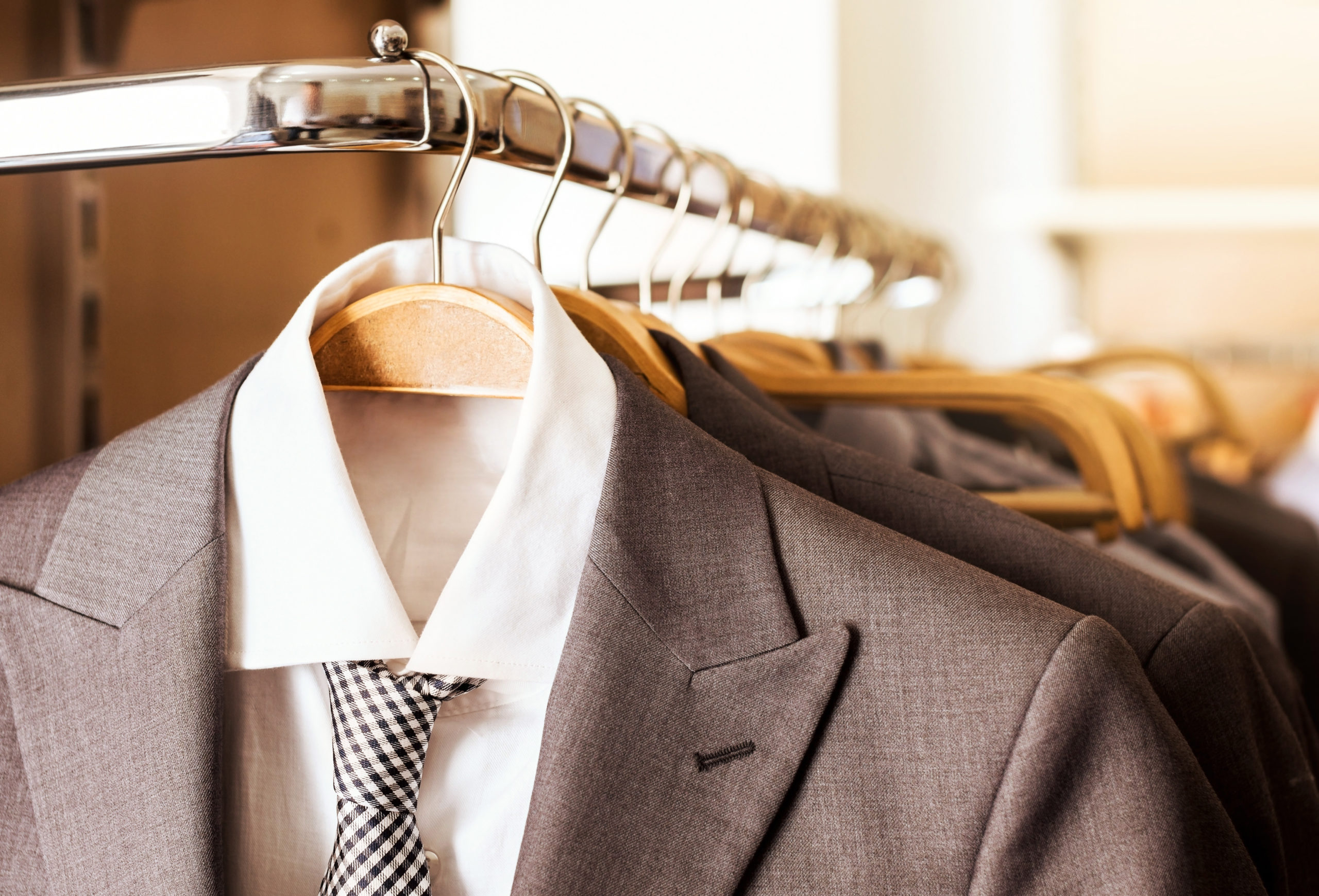 Mens suits and formal shirts on wooden hangers in a clothes store