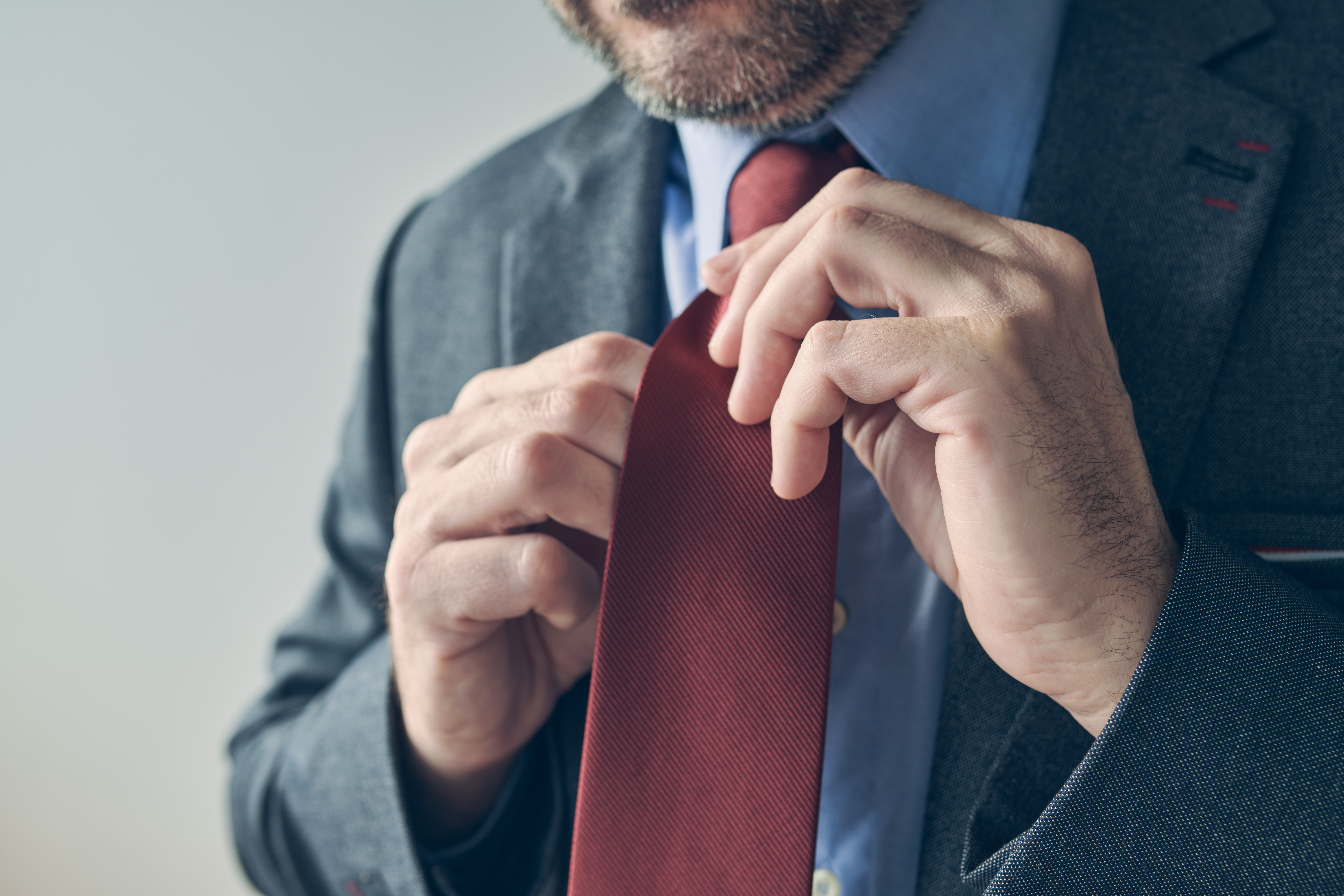 Businessman in elegant suit tying a red necktie